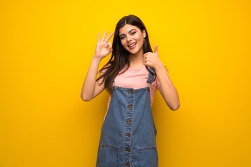 Obraz na płótnie Canvas Teenager girl over yellow wall showing ok sign with and giving a thumb up gesture