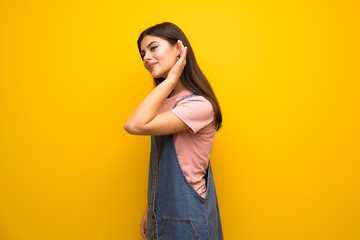 Teenager girl over yellow wall listening to something by putting hand on the ear