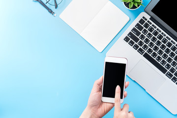 A woman is holding a smartphone isolated with a minimal blue desk, concept of online shopping payment, internet work at home, e-commerce, copy space, flat lay, top view, mock up