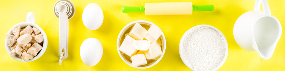 Baking ingredients and tools on trendy bright yellow background - flour, eggs, sugar, milk, butter, layout, flatlay top view copy space banner