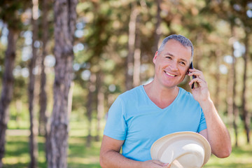 Happy man talking over phone on a bright sunny day and looking up. Smiling mature man using mobile...