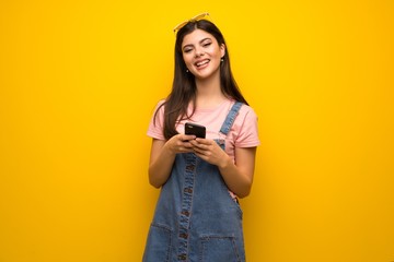 Teenager girl over yellow wall sending a message with the mobile