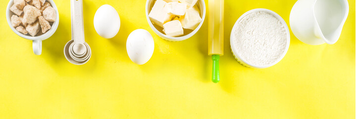 Baking ingredients and tools on trendy bright yellow background - flour, eggs, sugar, milk, butter, layout, flatlay top view copy space banner