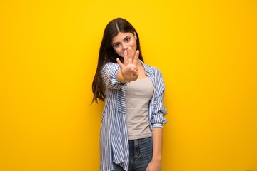 Teenager girl over yellow wall happy and counting four with fingers