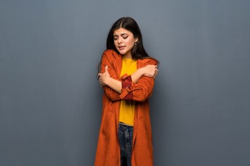 Teenager girl with coat over grey wall freezing