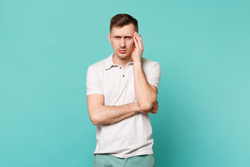 Tired disconcerted young man in casual clothes having headache, putting hands on temple isolated on blue turquoise background in studio. People sincere emotions, lifestyle concept. Mock up copy space.