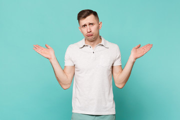Portrait of confused young man in casual clothes standing, spreading hands isolated on blue turquoise wall background. People sincere emotions, lifestyle concept. Mock up copy space. Advertising area.