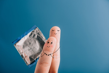 cropped view of happy couple of fingers hugging and holding condom isolated on blue