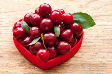 Cherry basket in red bowl. Cherry with leaves in heart. Fresh sweet cherries