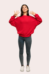 A full-length shot of a Teenager girl with red sweater counting nine with fingers over isolated background