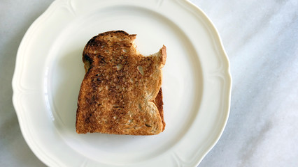 Toast bread bitten off at the top corner, on a white plate on top of marble counter.