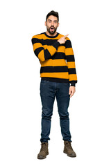 Fototapeta premium Full-length shot of Handsome man with striped sweater surprised and pointing side on isolated white background