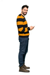 Full-length shot of Handsome man with striped sweater sending a message with the mobile on isolated white background