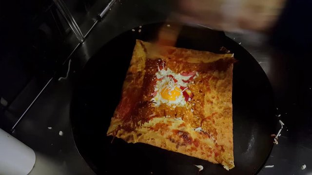 Top view of a cook preparing a crepe with cheese, Turkish sauge (sucuk) and egg.