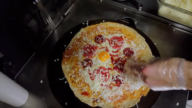 Top view of a cook preparing a crepe with cheese, Turkish sauge (sucuk) and egg.