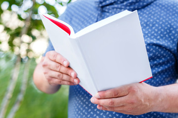 Man weared in a blue shirt holds open white empty book outdoors. Hands closeup.