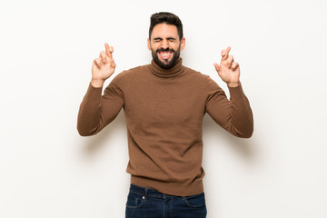 Handsome man over white wall with fingers crossing and wishing the best