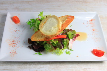 plate of warm goat cheese toast with lettuce salad in french restaurant