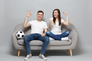 Fun couple woman man football fans cheer up support favorite team holding bitcoin, future currency, showing thumb up, OK sign isolated on grey wall background. Sport family leisure lifestyle concept.