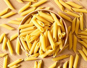 Delicious pasta or penne noodles on a wooden table background. Top view scene, healthy eating or healthy lifestyle. Penne pasta or macaroni in a wooden bowl, italian cuisine.