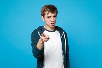 Portrait of displeased young man in casual clothes pointing index finger on camera isolated on blue...