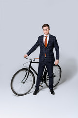 stylish businessman in suit standing with bicycle on grey