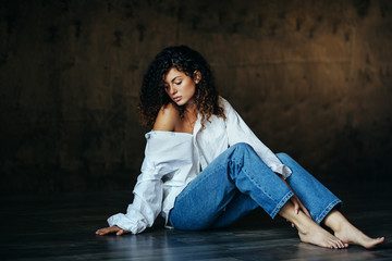 Portrait of a beautiful young girl in a dark studio. Curly hair. Unbuttoned shirt