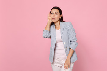 Portrait of curious young woman in striped jacket eavesdrop with hearing gesture, looking aside isolated on pink pastel wall background. People sincere emotions, lifestyle concept. Mock up copy space.