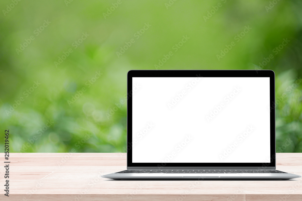 Aufkleber empty wooden table with blank screen laptop on green blurred abstract background from foliage backgr