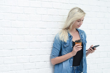 Young businesswoman useing smartphone and holding coffee cup with white wall background, copy space.