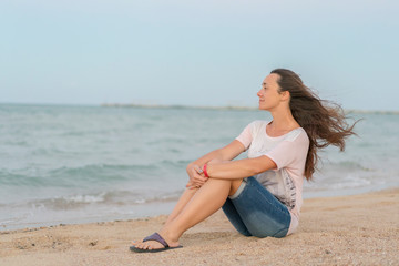 Fototapeta na wymiar Beautiful girl sitting on the beach. Middle aged woman resting at beach near the sea. young, beautiful woman with long flowing hair on the beach