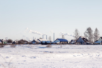 Bright winter landscape with blue sky in the spring sun and in the background village and industrial pipes with smoke in the environment. Сoncept of pollution and global warming.