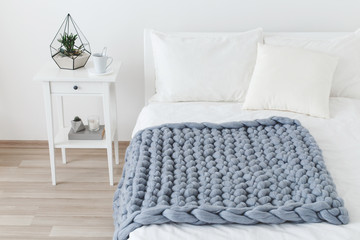 Bed with white linen and grey knitted woolen merino chunky blanket. Light stylish cozy scandinavian...