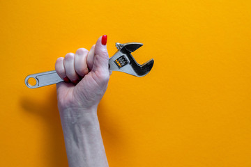hand of a young woman holding a chrome key, red nail polish, close-up on a yellow background