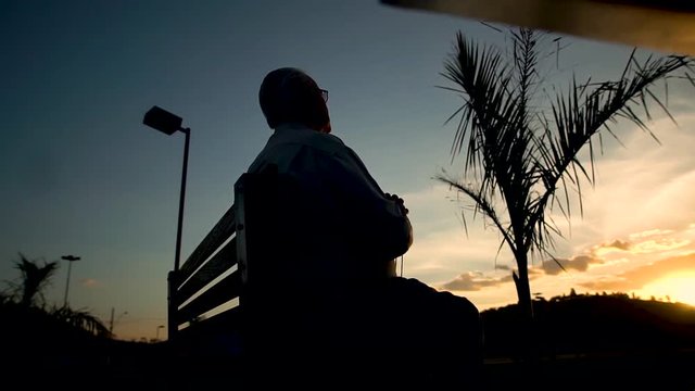 Homem sentado em um banco vendo o por do sol