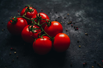 Beautiful fresh tomatoes on a branch isolated on black table background. Ripe organic vegetables. Vegetarian food