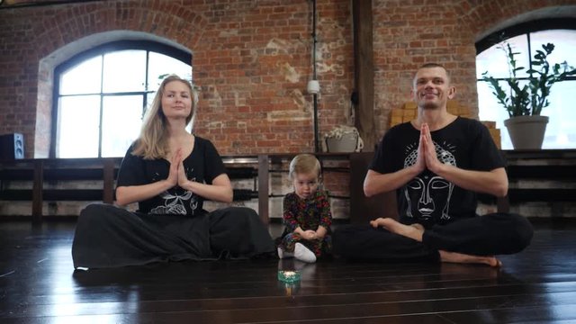 Yoga family father mother and child baby daughter namaste sit in pose on a floor