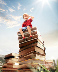 Little boy sitting on the tower made of big books. Childhood dreams, reading and education concept....