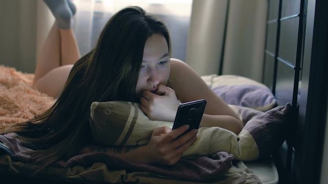 Young brunette woman in bed uses the phone. She is lying in her underwear on the bed.