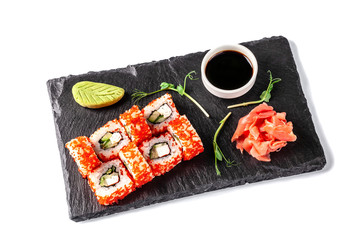 Concept of Japanese cuisine. Roll with crab sticks, cucumber and celery, with red caviar. Near soy sauce, ginger and wasabi. Modern serving dishes in the restaurant on a black slate blackboard. ??????