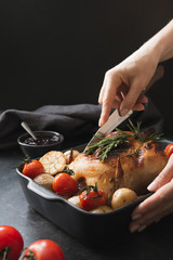 Roasted chicken with vegetables on black. Woman cuts chicken.