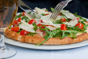 Pizza with tomatoes. cheese and ruccola salad in restaurant in Rome, Italy. With knife and fork