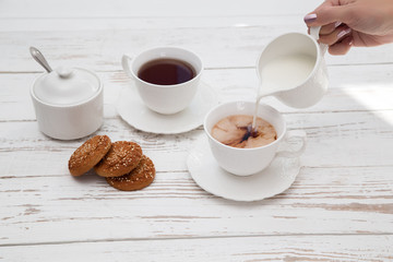 hands pours cream in cup of tea on wooden white table