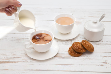 hands pours cream in cup of tea on wooden white table