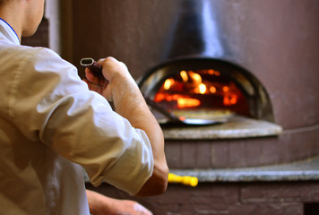 Pizza maker in pizzeria makes pizza in wood-fired oven