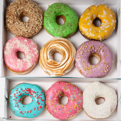 Colorful donuts in an open box on a wooden table. Top view