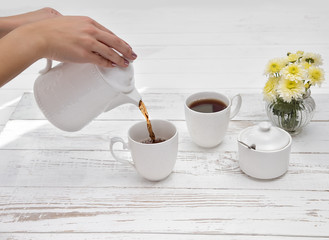 hands pours tea in cup of tea on wooden white table