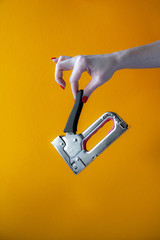 hand of a young woman holding a metal stapler, close-up on a yellow background, vertical shot