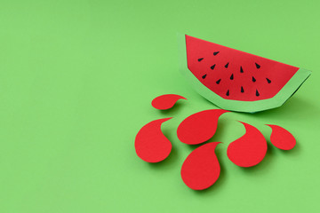 Paper watermelon slice with splashes on green pastel background. Creative idea. Art food concept.