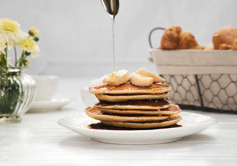 pouring honey onto tasty pancakes on wooden table, closeup